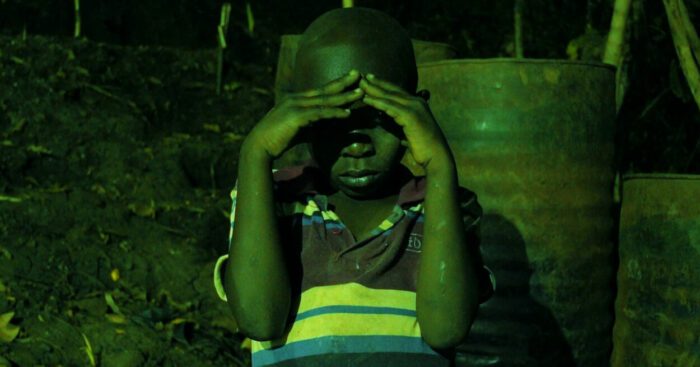 A small Ugandan boy covers his eyes to avoid a green fluorescent light.