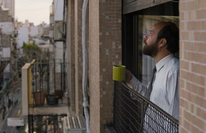 Moran looks out an apartment window, holding a coffee cup.