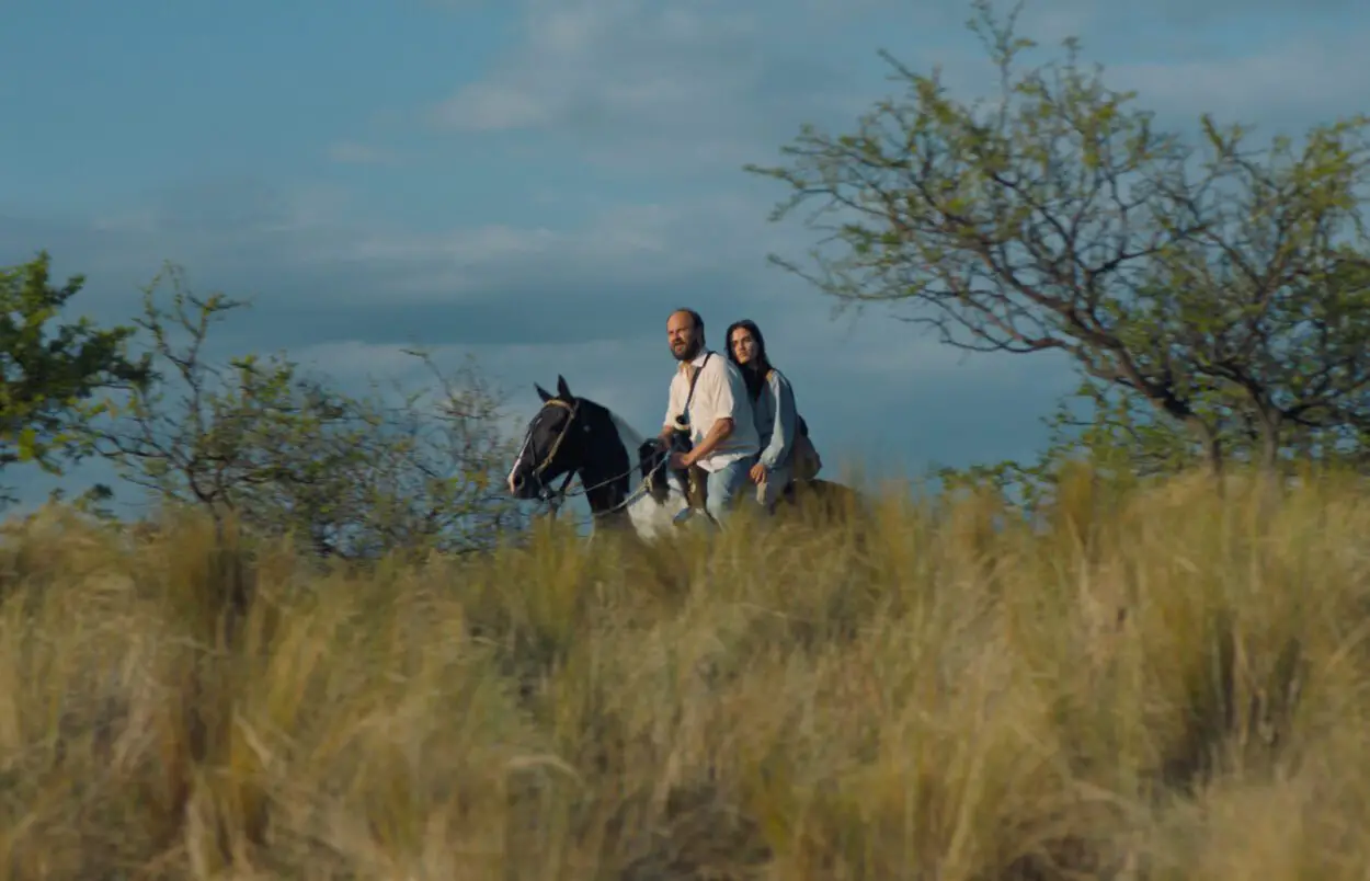 A man and woman ride through a field on horseback.