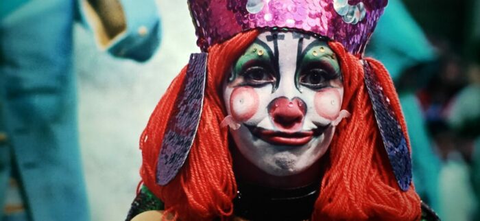 Valerie Jodorowsky as Sel in The Holy Mountain (1973). Sel is dressed as a ragdoll clown in full face paint wearing a purple bishop's miter. Screen capture off of Amazon.