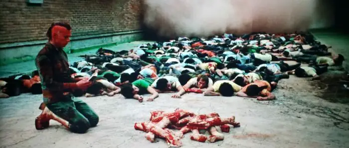 Richard Rutowsky as Axon in The Holy Mountain (1973). Axon kneels in the street wearing a paramilitary police uniform while surrounded by bloody dead bodies. Screen capture off of Amazon.