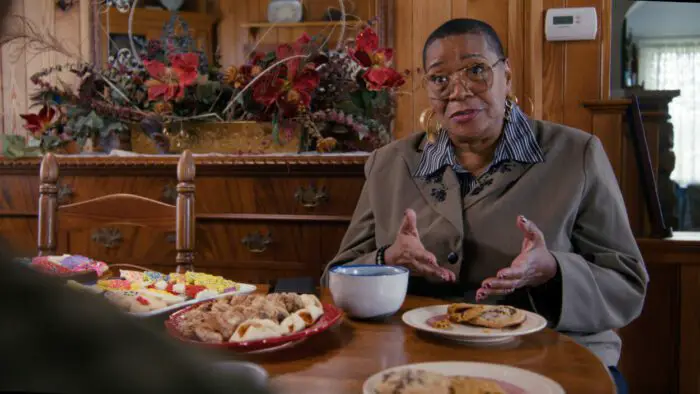 Marsha Warfield as banker Andrea at a table enjoying Christmas cookies in A Holiday I Do (2023).