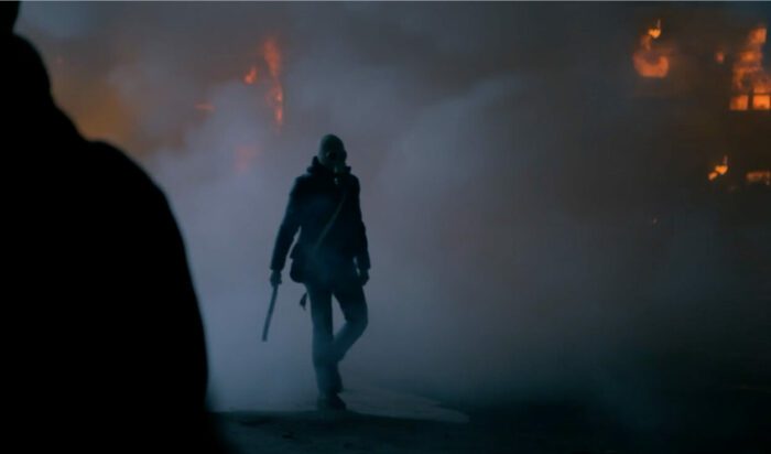 An armed figure emerges from a grey cloud of dust and smoke.