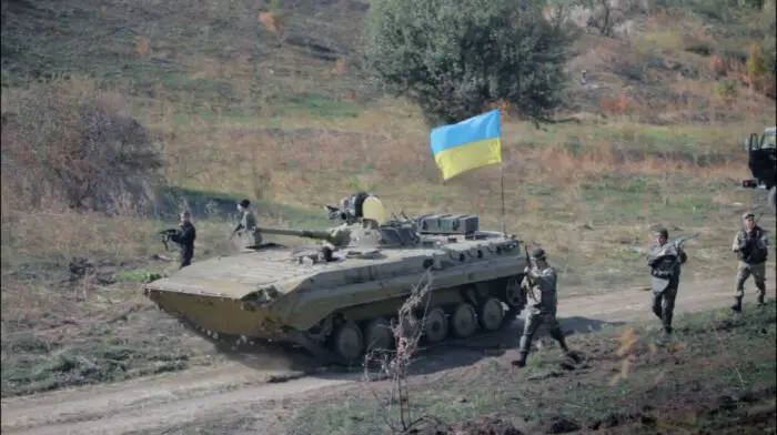 Ukrainian soldiers march alongside a tank.