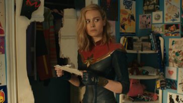 Captain Marvel stands surprised in a teenager's bedroom in The Marvels.