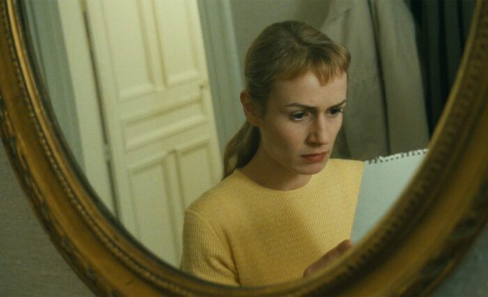 Sophie struggles to read a letter, framed by a mirror.