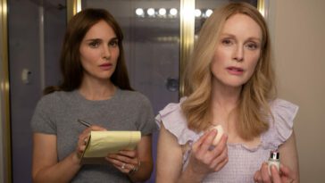 Elizabeth (Natalie Portman) studies Gracie (Julianne Moore) as she applies makeup in a bathroom. Elizabeth holds a notepad in the well-lit bathroom.