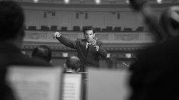 A man is scene through musicians conducting an orchestra in Maestro.