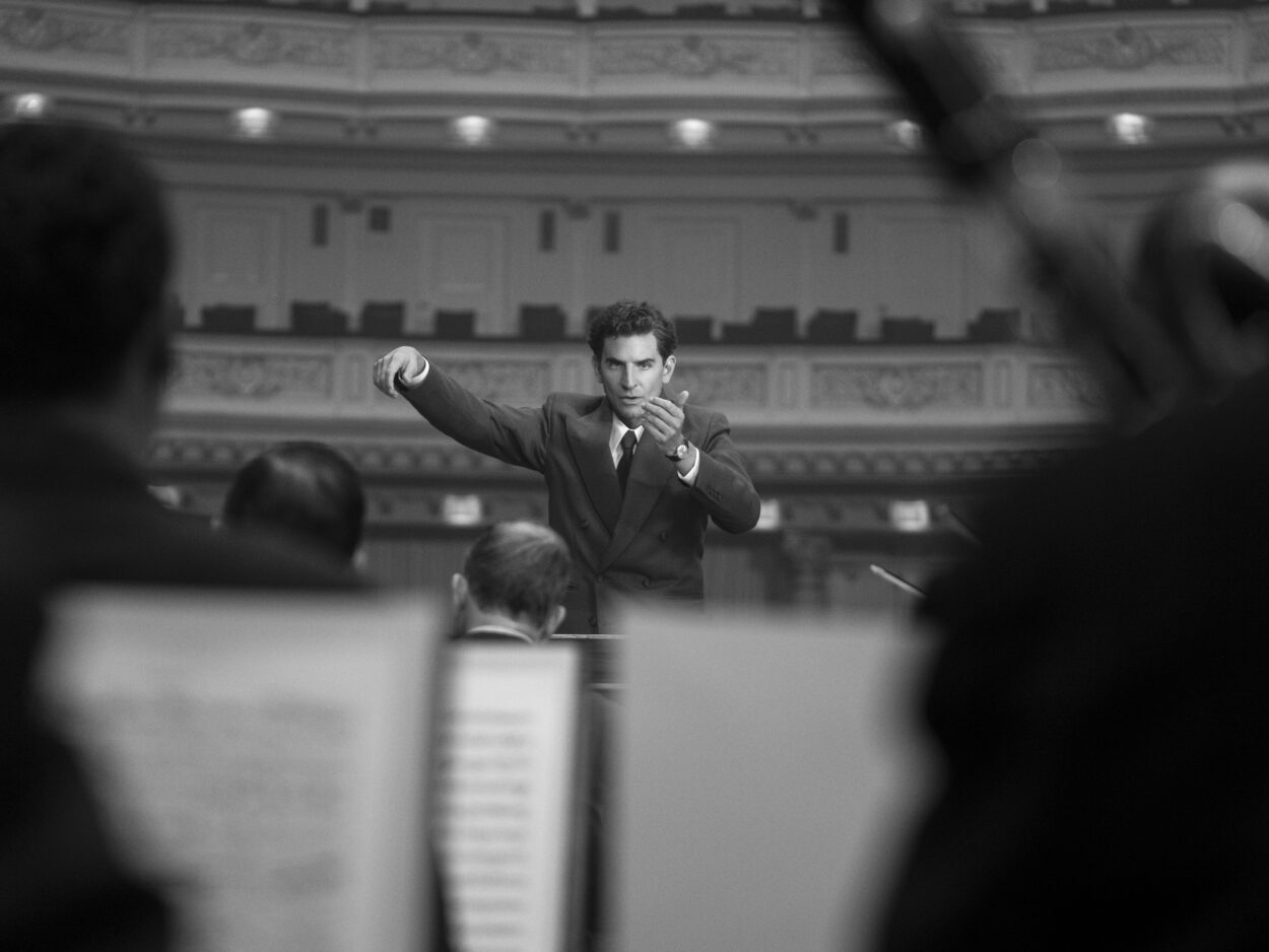 A man is scene through musicians conducting an orchestra in Maestro.