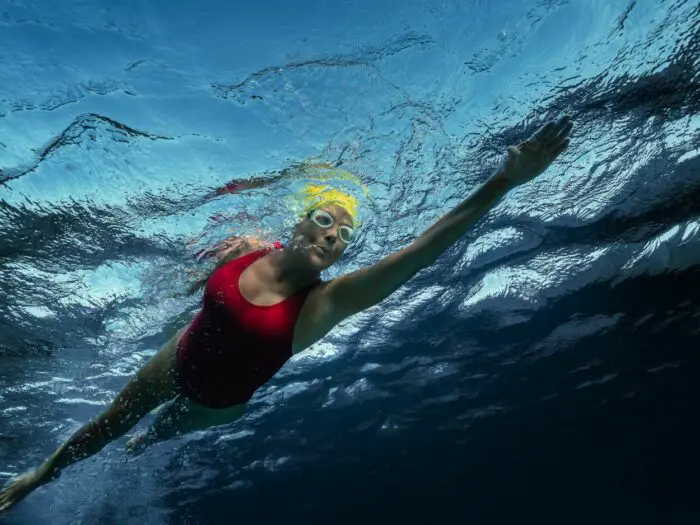 A woman is seen from underwater swimming forward.