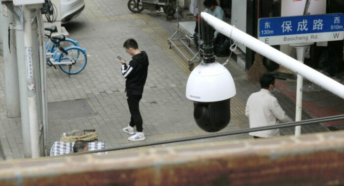 A man in China looks at his phone while neighbors observe his activity.