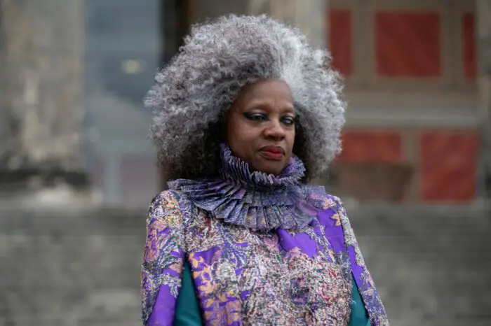 Dr. Volumnia Gaul (Viola Davis) has a blue glass eye, mad scientist-esque gray and white hair, and a decorative and elaborate purple outfit outside. 