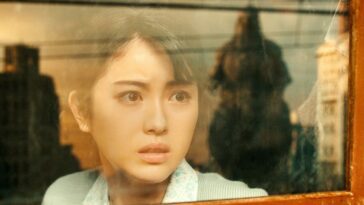 Noriko stares out the wind of a train, horrified by Godzilla's mammoth form