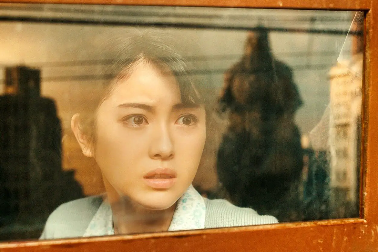 Noriko stares out the wind of a train, horrified by Godzilla's mammoth form