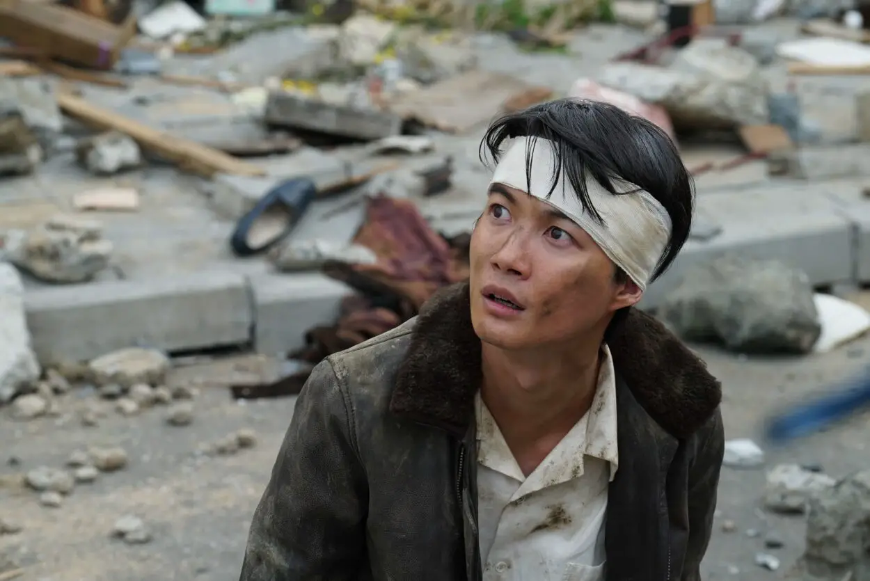Shikishama wears a head bandage and looks up at the destruction all around him