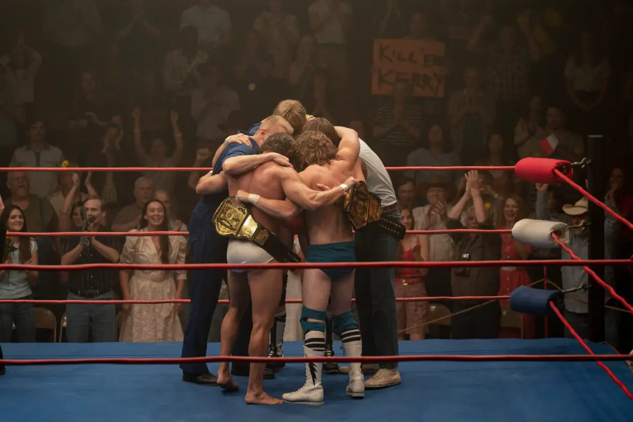 A group of brothers and family members huddle in a wrestling ring.