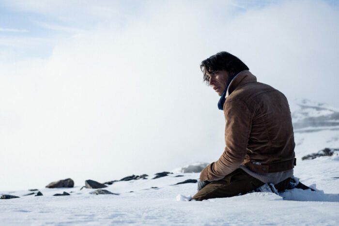 A man kneels near wreckage and bodies in Society of the Snow