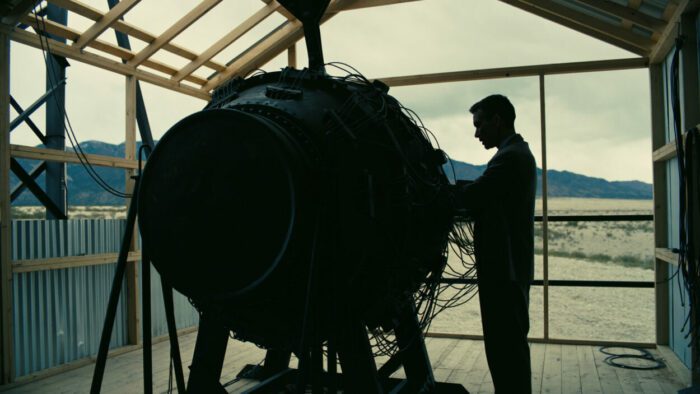 Oppenheimer, in silhouette, placing his hand on the Trinity bomb.
