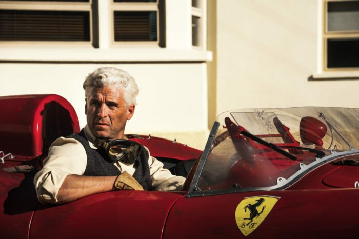 Patrick Dempsey as Piero Taruffi in Ferrari (2023). Photo credit Lorenzo Sisti. Owner EF Neon. Silver haired Patrick Dempsey sits in a red racecar bearing the Ferrari logo, a horse rearing up on its hindlegs.