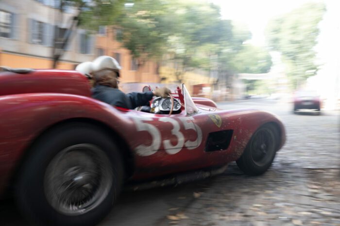 Photo from the set of Ferrari (2023). Photo credit Eros Hoagland. Owner EF Neon. Photo shows a sleek, compact red racing car, the Ferrari 315 S, flying down a cobblestone street.
