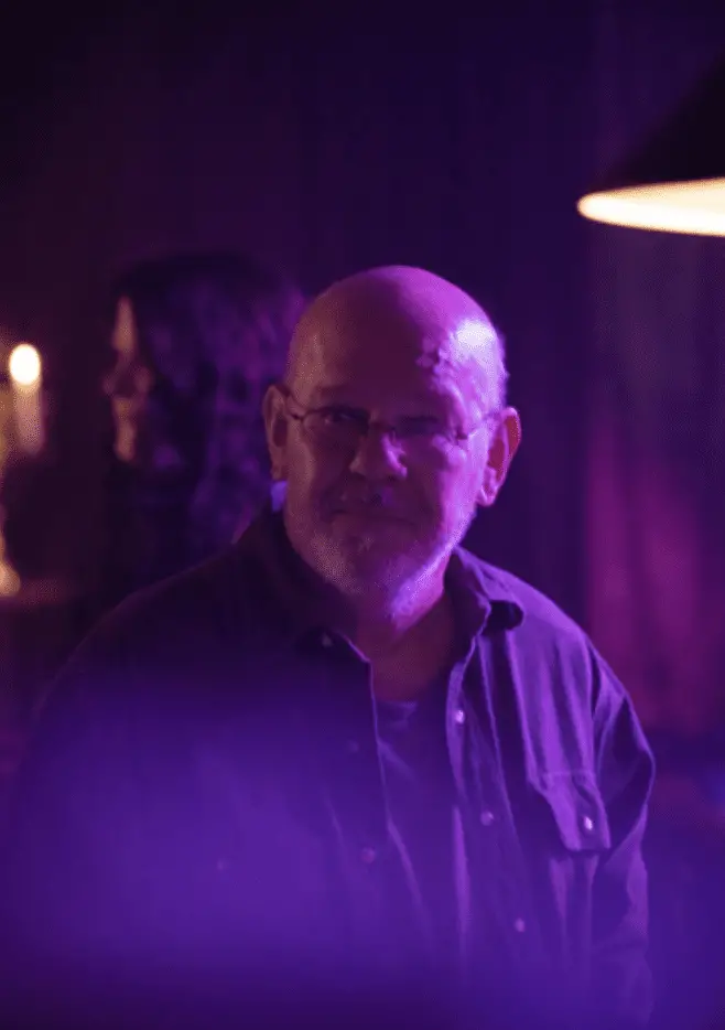 Charles Martin Smith as Red, covered in purple light in a bar.