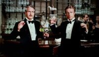 Paul Newman and Robert Redford as Henry Gondorff and Johnny Hooker in The Sting (1973). Dressed in tuxedoes, the two men stand in a fancy bar, hands raised as the police raid their illegal betting parlor. Screen capture off the 100th Anniversary Collectors' Series Blu-ray.
