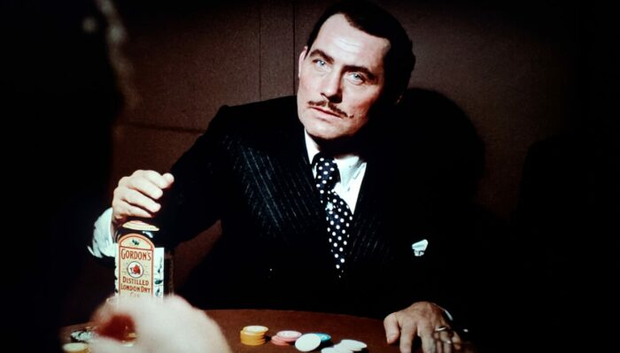 Robert Shaw as Doyle Lonnegan in The Sting (1973). Lonnegan sits at a poker table glaring while angrily holding a gin bottle. Screen capture off the Universal 100th Anniversary Collectors' Series Blu-ray.