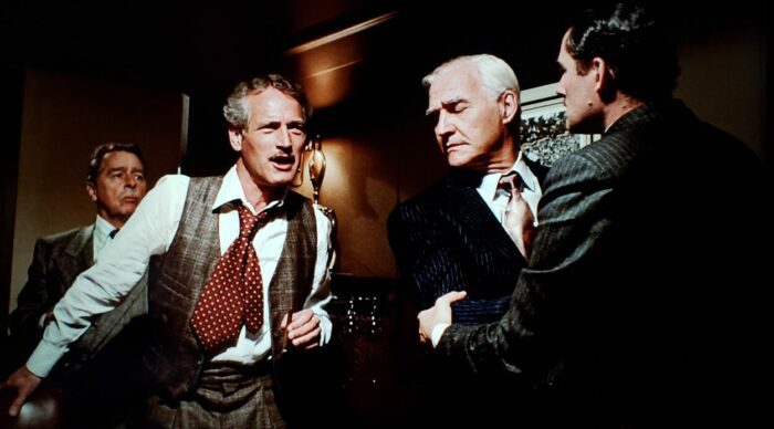 [L to R] Robert Brubaker, Paul Newman, Clarke Gordon, Robert Shaw as Bill Clayton, Henry Gondorff, Mr. Lombard, and Doyle Lonnegan. in The Sting (1973). Newman and Shaw standing around a poker table arguing and being restrained from fighting by the others. Screen capture off the Universal 100th Anniversary Collectors' Series Blu-ray.
