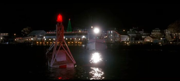 Police boat approaching a log trapped on a buoy in dark water. Jaws: The Revenge (1987). Screen capture off Netflix.