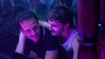 Adam and Andrew embrace, bathed in the purple light of a club.