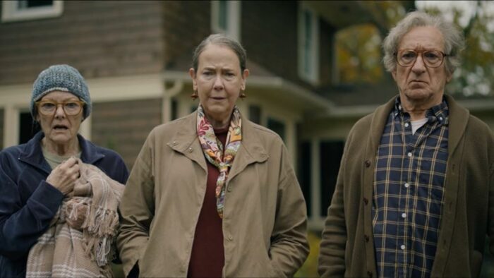 Image from Jules showing three people (Jane Curtin, Harriet Sansom Harris, Ben Kingsley) standing side-by-side looking forward. A house in the background. 