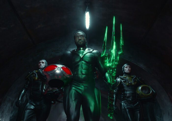 YAHYA ABDUL-MATEEN II as Black Manta in Warner Bros. Pictures’ action adventure “Aquaman and the Lost Kingdom,” a Warner Bros. Pictures release. Black Manta flanked by his henchmen strides down a dark hall carrying a black trident eerily glowing emerald green.