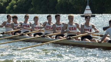 A eight-man team of rowers pulls foward in a race in The Boys in the Boat.