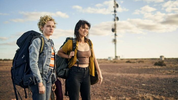 Image depicting Julia Garner and Jessica Henwick from THE ROYAL HOTEL. Their characters are carrying backpacks and looking out into the distance of the desert.
