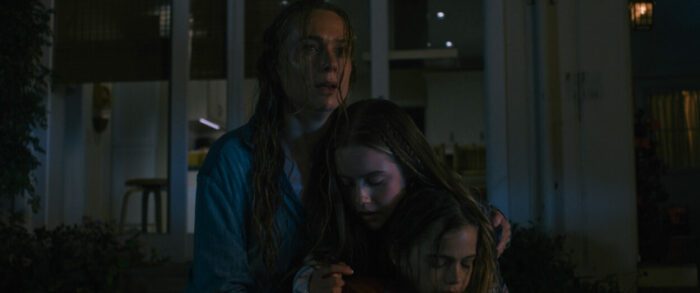 (from left) Eve Waller (Kerry Condon), Izzy Waller (Amélie Hoeferle) and Elliot Waller (Gavin Warren) in Night Swim, directed by Bryce McGuire. © 2023 Universal Studios. All Rights Reserved. Eve Waller and her two children standing dripping wet beside the pool at night, all looking shook and frightened, yet clinging to one another for relief.
