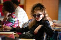 Lisa in her goth outfit, sit at a school desk