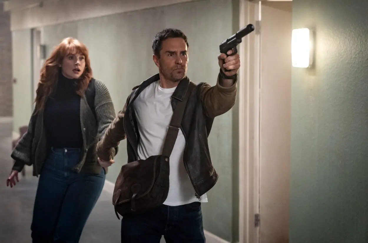 (from left) Elly Conway (Bryce Dallas Howard) and Aidan (Sam Rockwell) in Argylle, directed by Matthew Vaughn. Universal Pictures; Apple Original Films; and MARV. Real life spy wielding a silenced pistol leads author Elly Conway through a dangerous hall.