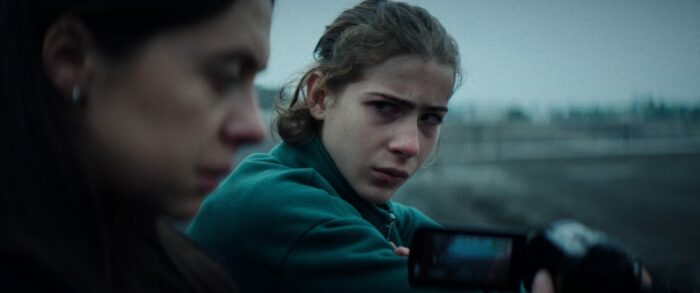 A teenage boy looks towards a woman telling a story in Cold Copy