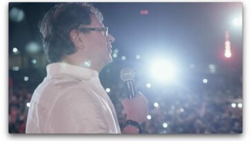 Gustavo Petro at a campaign rally, with a large crowd and flashing lights behind him.