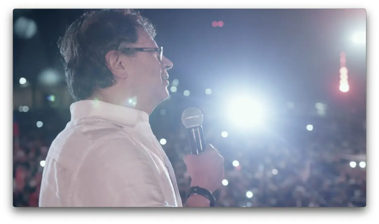 Gustavo Petro at a campaign rally, with a large crowd and flashing lights behind him.