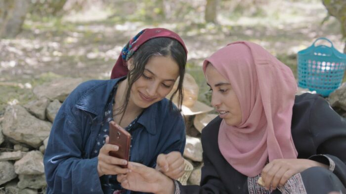 Two young female orchard workers share an image on a smartphone.