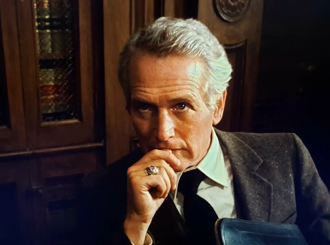 Paul Newman as Frank Galvin in The Verdict (1982). Screen capture off of Max. © 20th Century Fox. Galvin in a suit and tie sits softly glaring up at the camera.