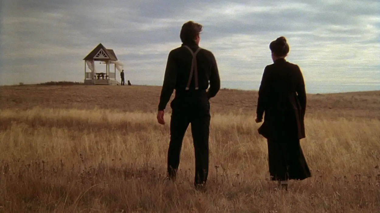 A scene from film Days of Heaven showing two people walking towards an isolated house in a field.