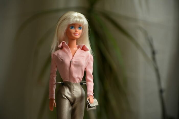 A blonde doll is wearing a pink jacket and leather pants.