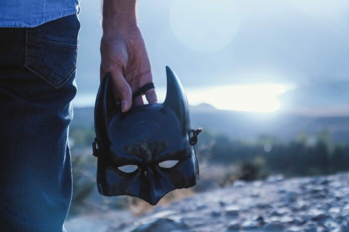 A man holds a Batman mask at his side.