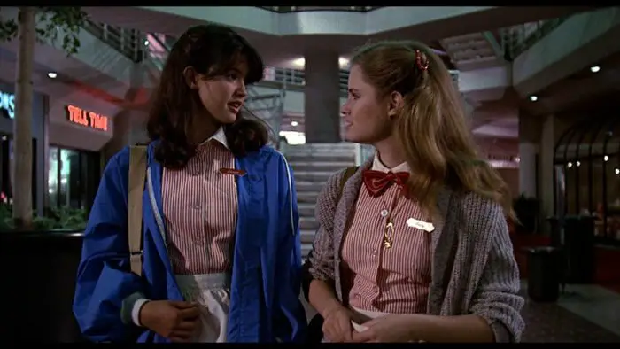 In a very 1980s mall backdrop, Stacy and Linda are walking out after work and stand talking to each other. 