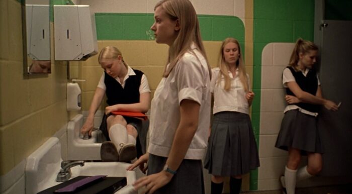Bonnie, Lux, Therese, and Mary are hanging out in the school bathroom. Lux is smoking a cigarette. 