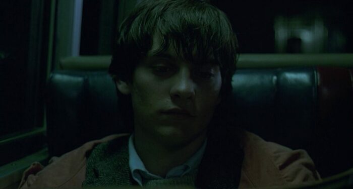 Paul is sitting in a dimly-lit train looking worn out. 