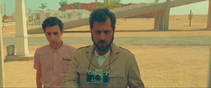 Augie (Jason Schwartzman) and Woodrow (Jake Ryan) are shown stranded in a small desert town with Augie's camera around his neck.