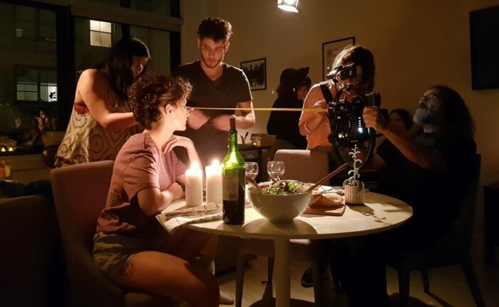 A behind-the-scenes image from the making of Aligned, with actors and crew assembled together around an intimately lit dining table.
